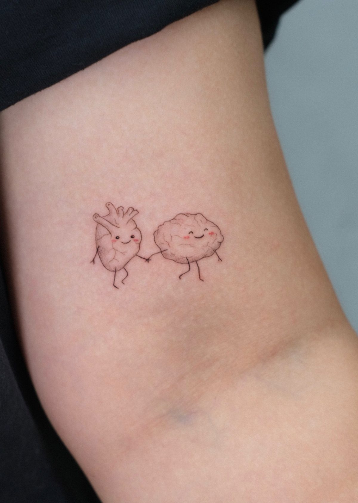 Anatomical heart and brain tattoos holding hands with smiling faces on skin