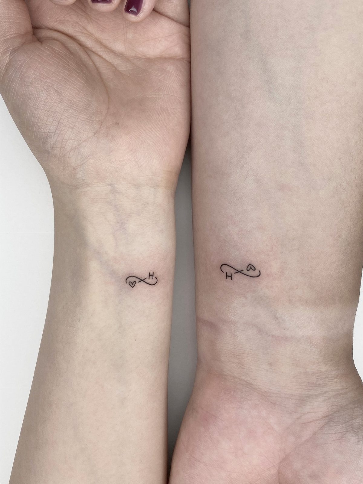 Two wrists with matching infinity symbol tattoos including a heart and letter H