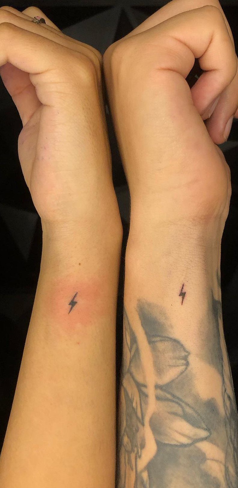 Two wrists side-by-side featuring matching small black lightning bolt tattoos.