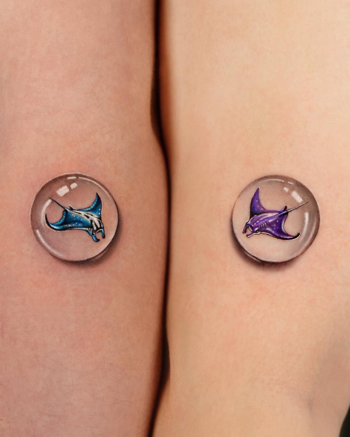 Two matching manta ray tattoos inside transparent bubbles on two people's arms.