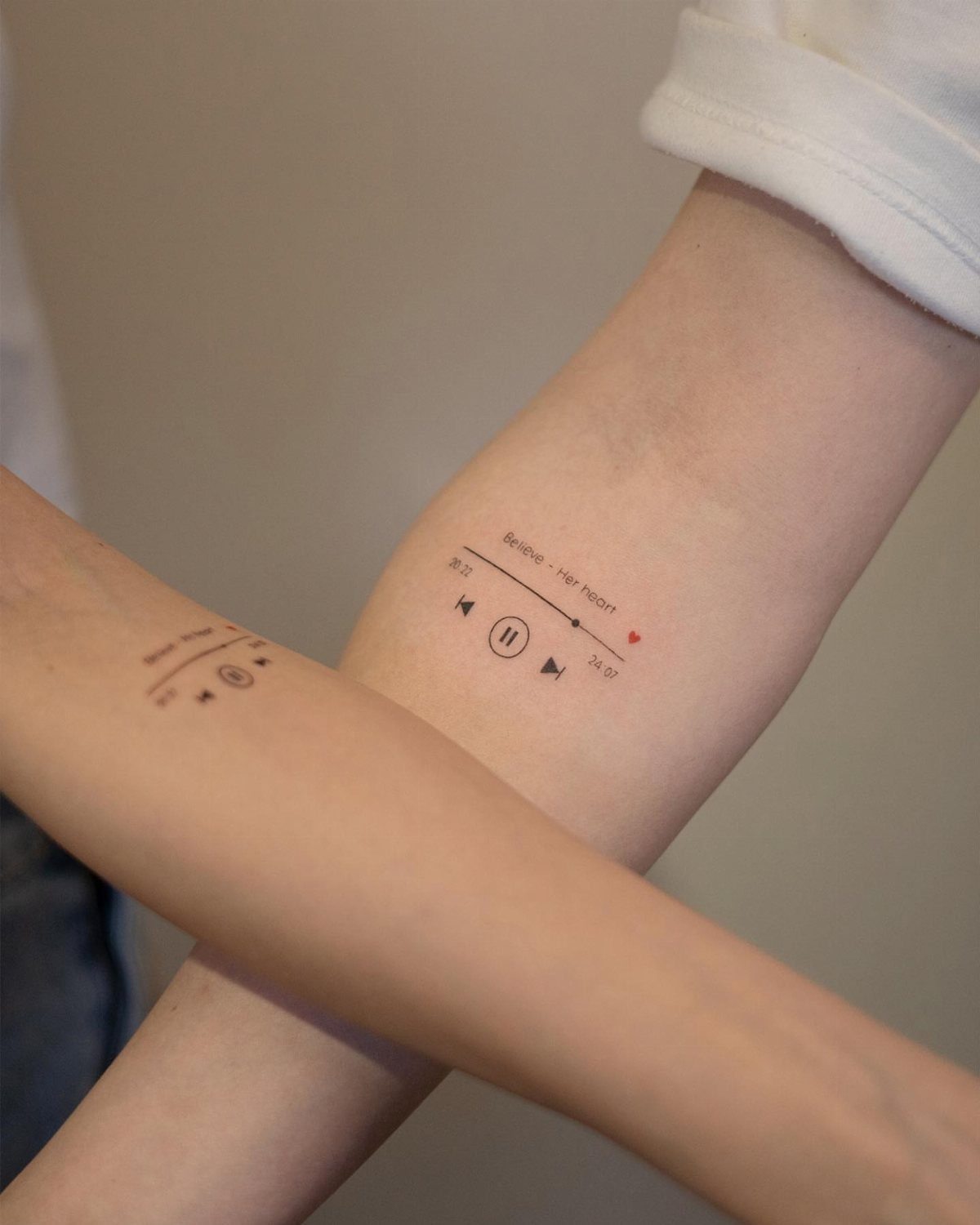 Two forearms with matching music player interface tattoos including play and pause buttons.
