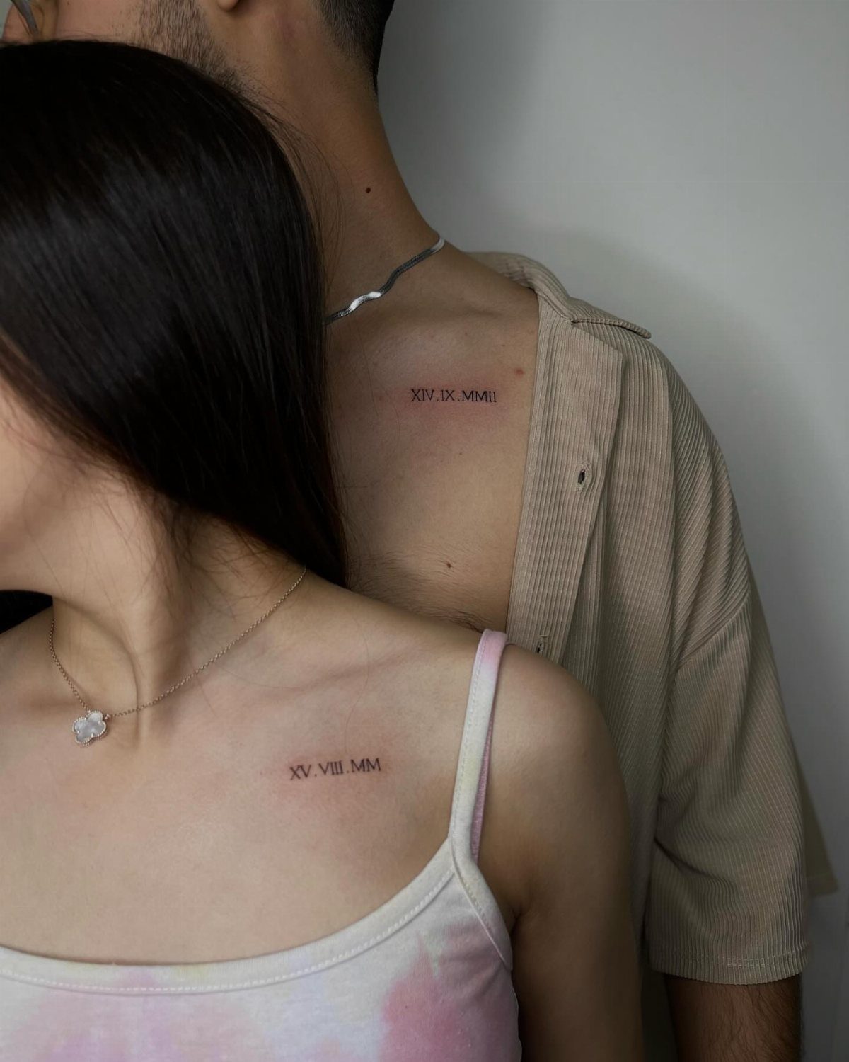 Couple with matching Roman numeral tattoos on their collarbones standing close together.