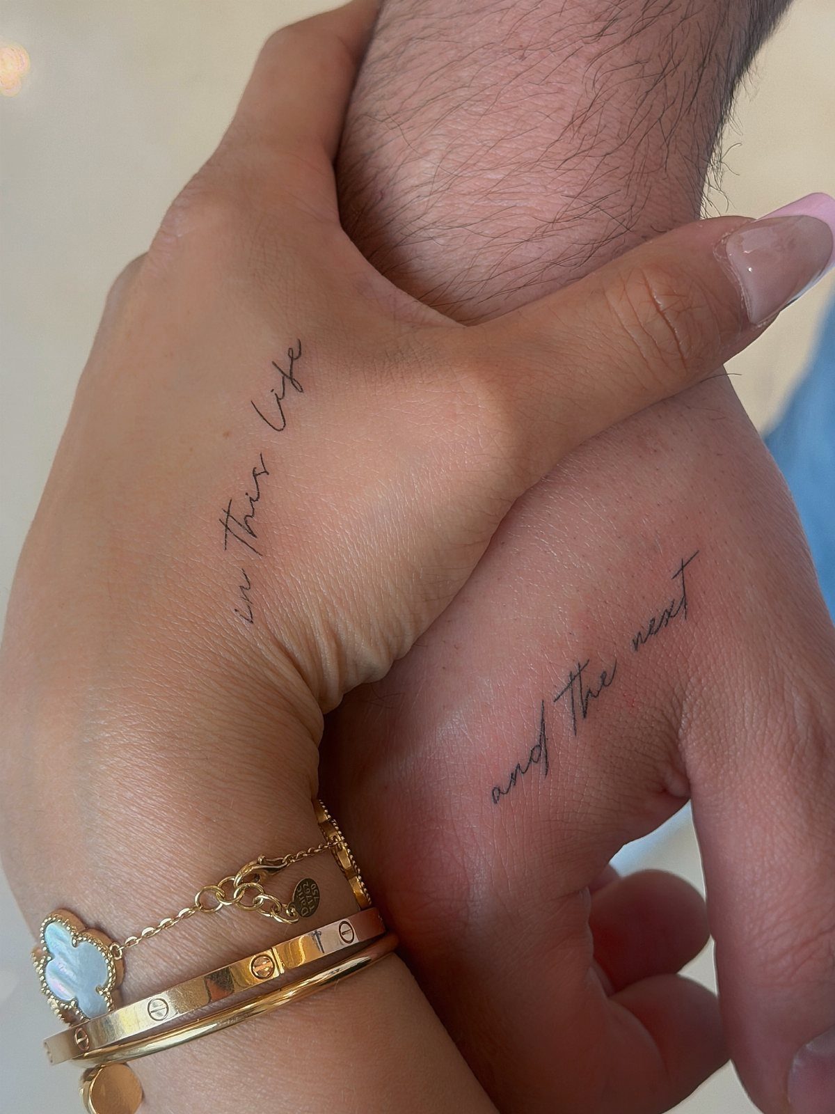 Two hands with matching script tattoos reading in this life and the next