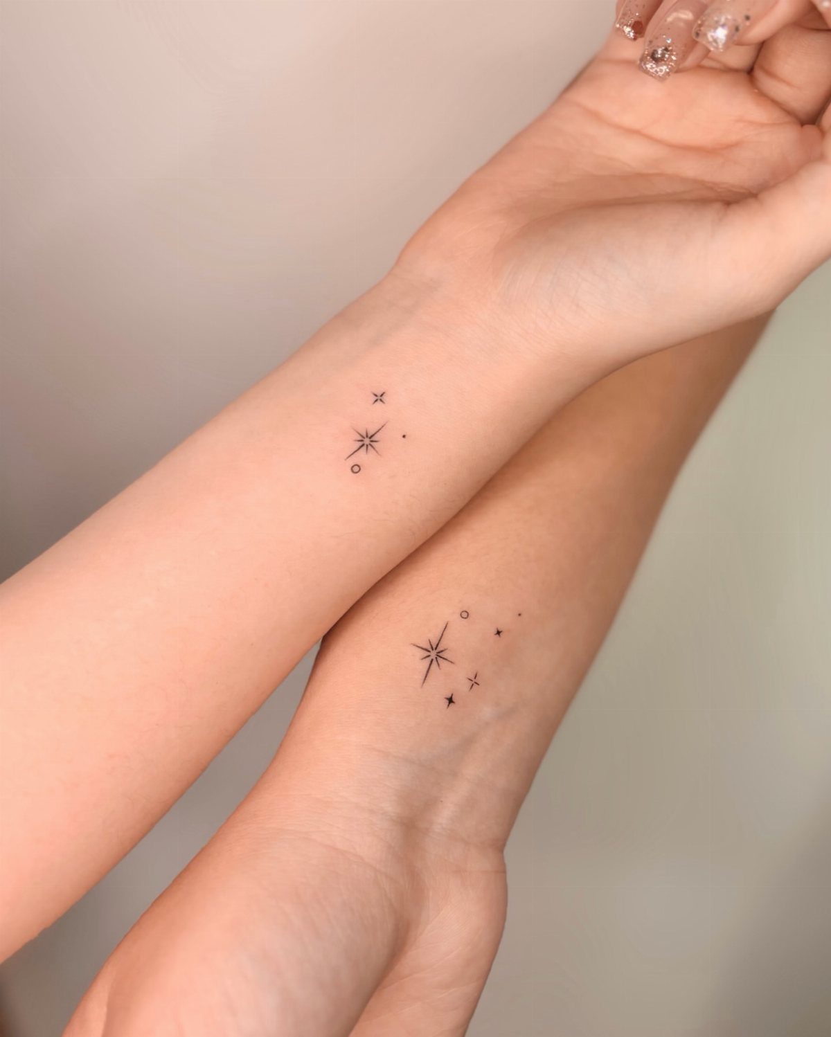 Two wrists with small minimalist star tattoos in black ink.