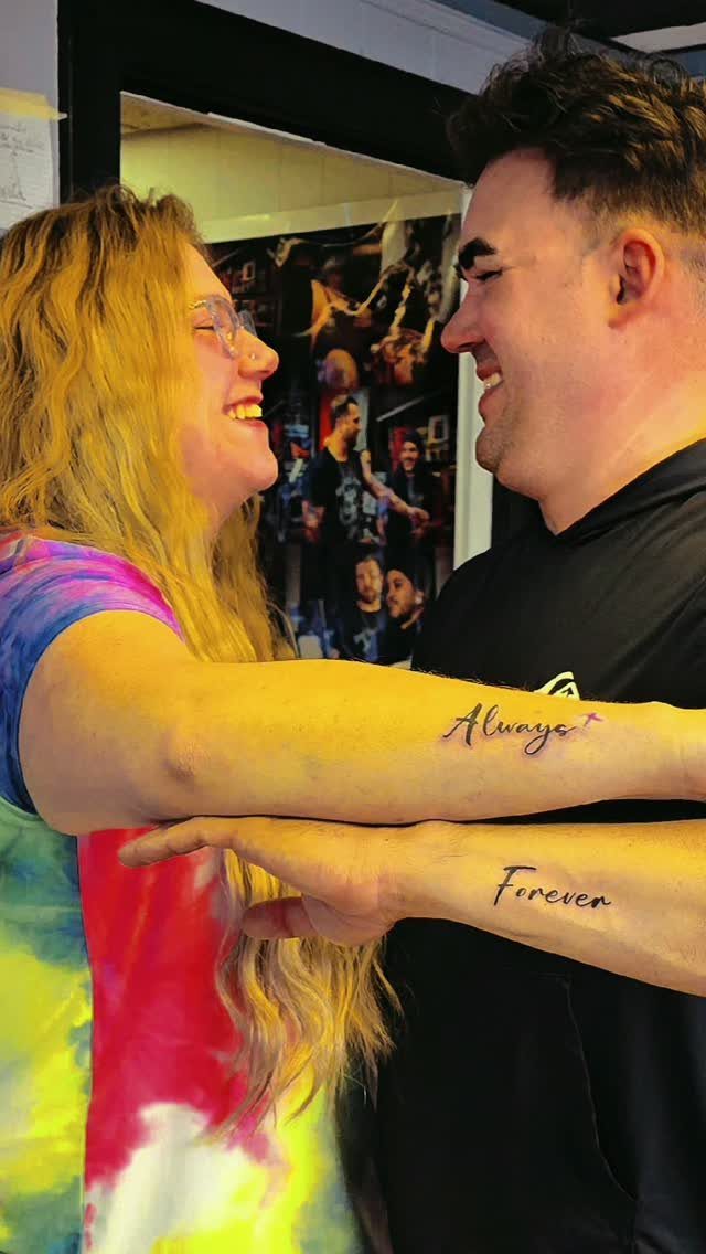 Couple smiling with matching 'Always' and 'Forever' tattoos on their forearms.