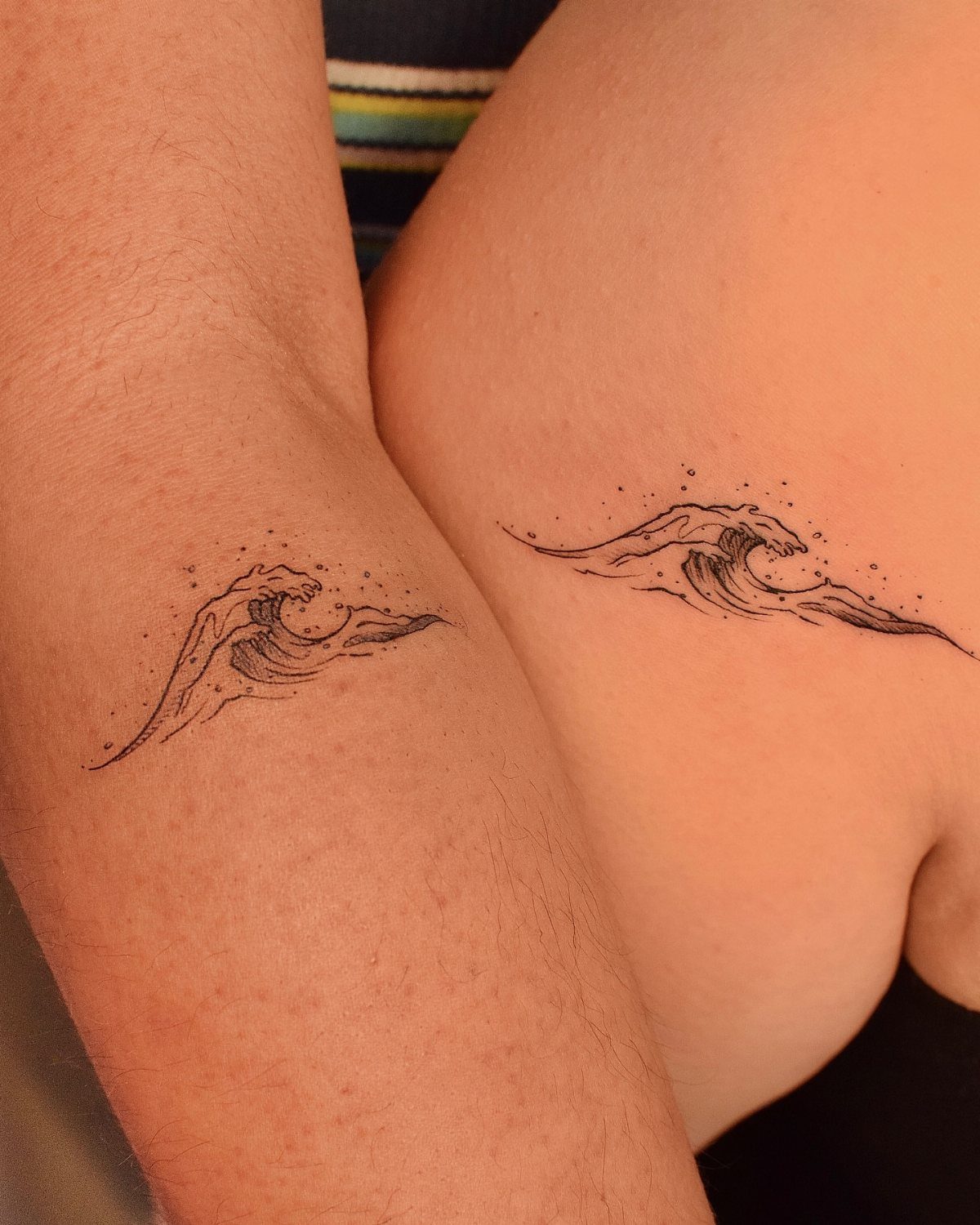 Matching small black ink ocean wave tattoos on an arm and a torso.