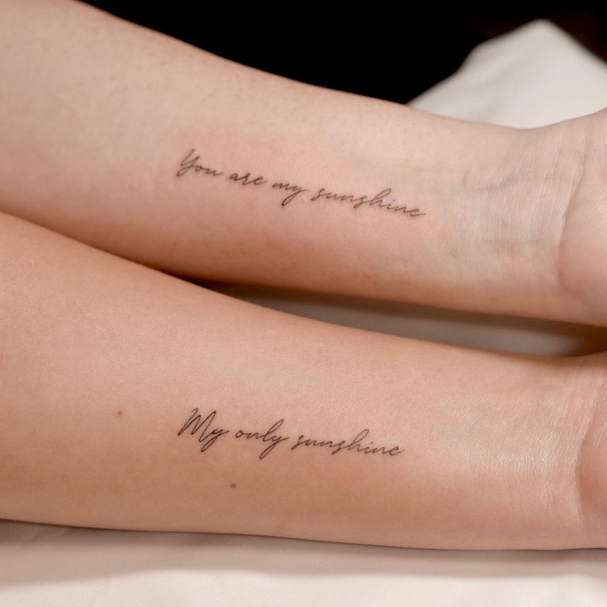 Two forearms with matching cursive tattoos reading You are my sunshine and My only sunshine.