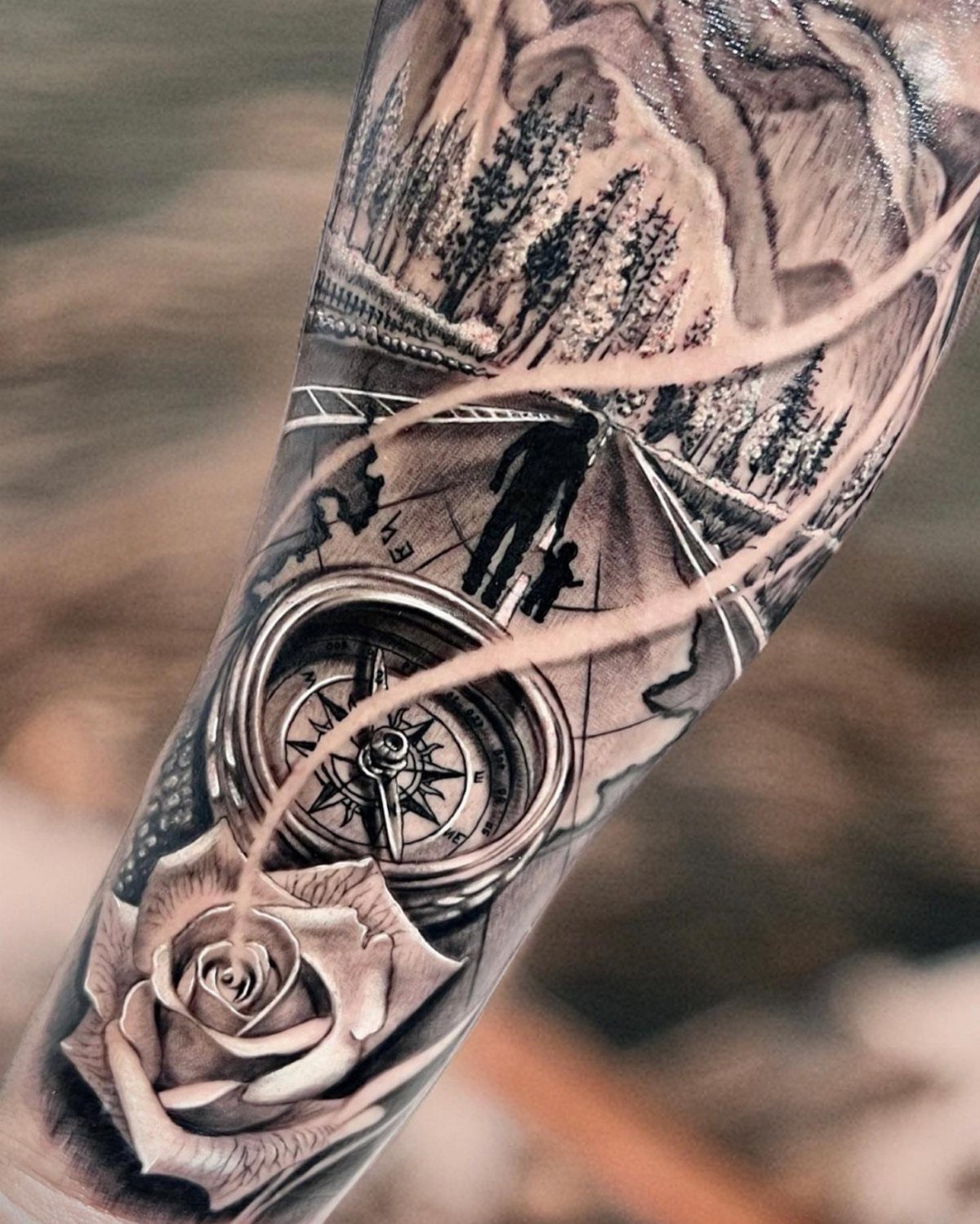 Detailed arm tattoo featuring a compass, a rose, and silhouettes of father and son.