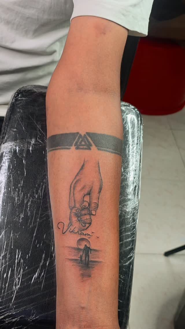 Tattoo of a large hand holding a small child's hand on a forearm