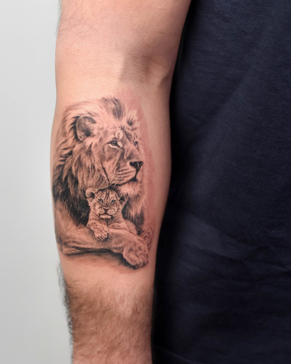 Lion and cub tattoo on a forearm in realistic black and grey ink