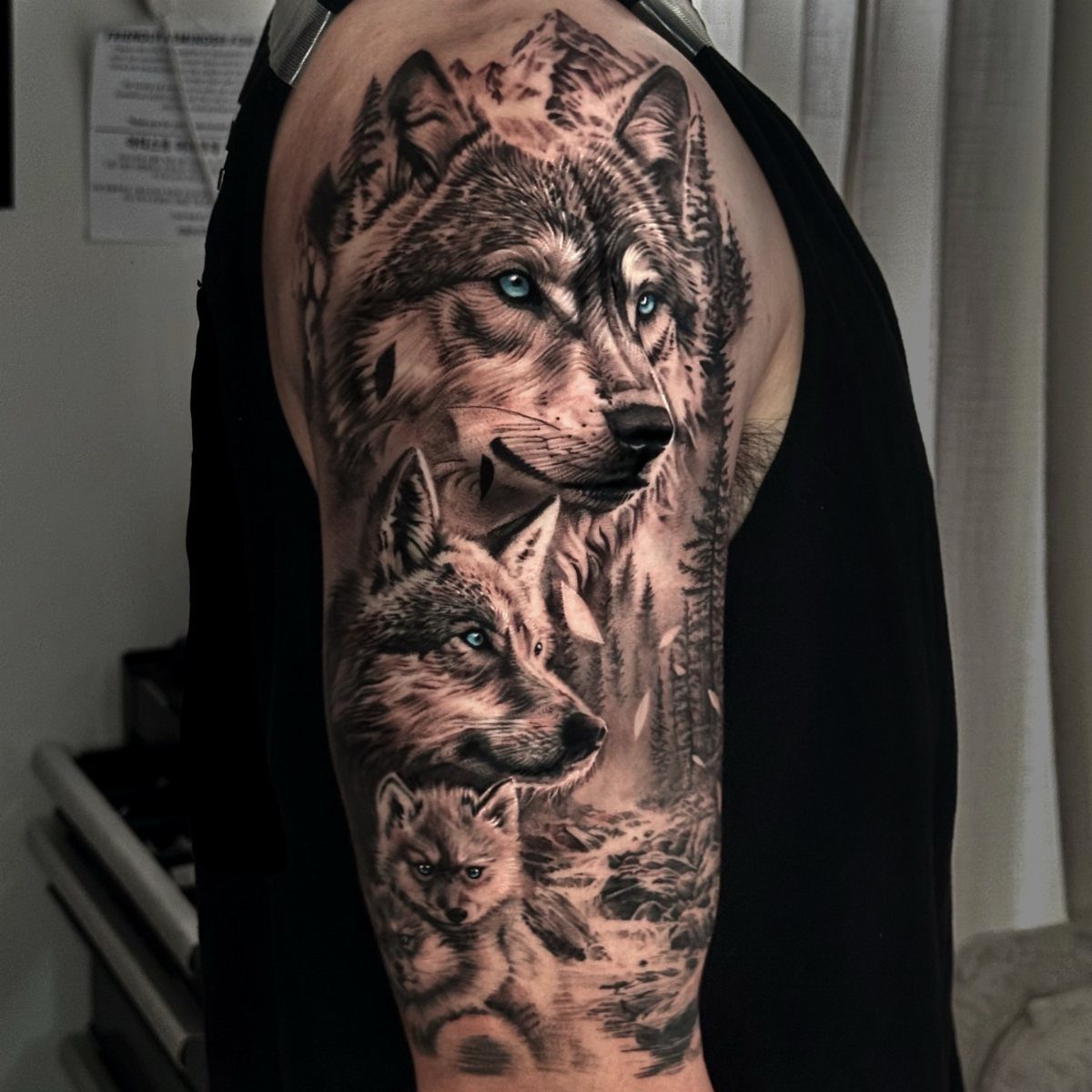 Wolf and cub tattoo on an arm with mountains and blue eyes.