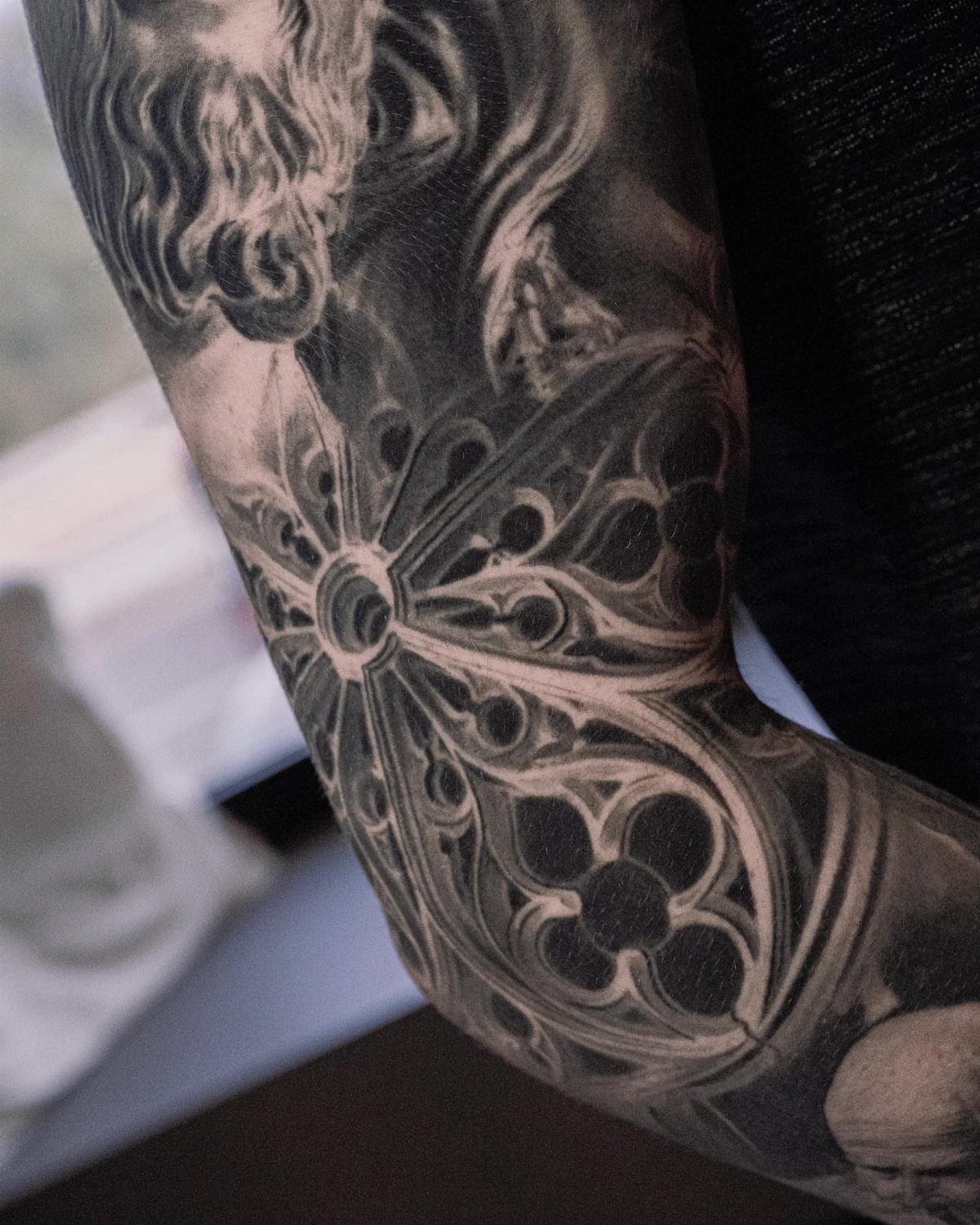 Black and grey tattoo of a gothic stained glass window on an arm