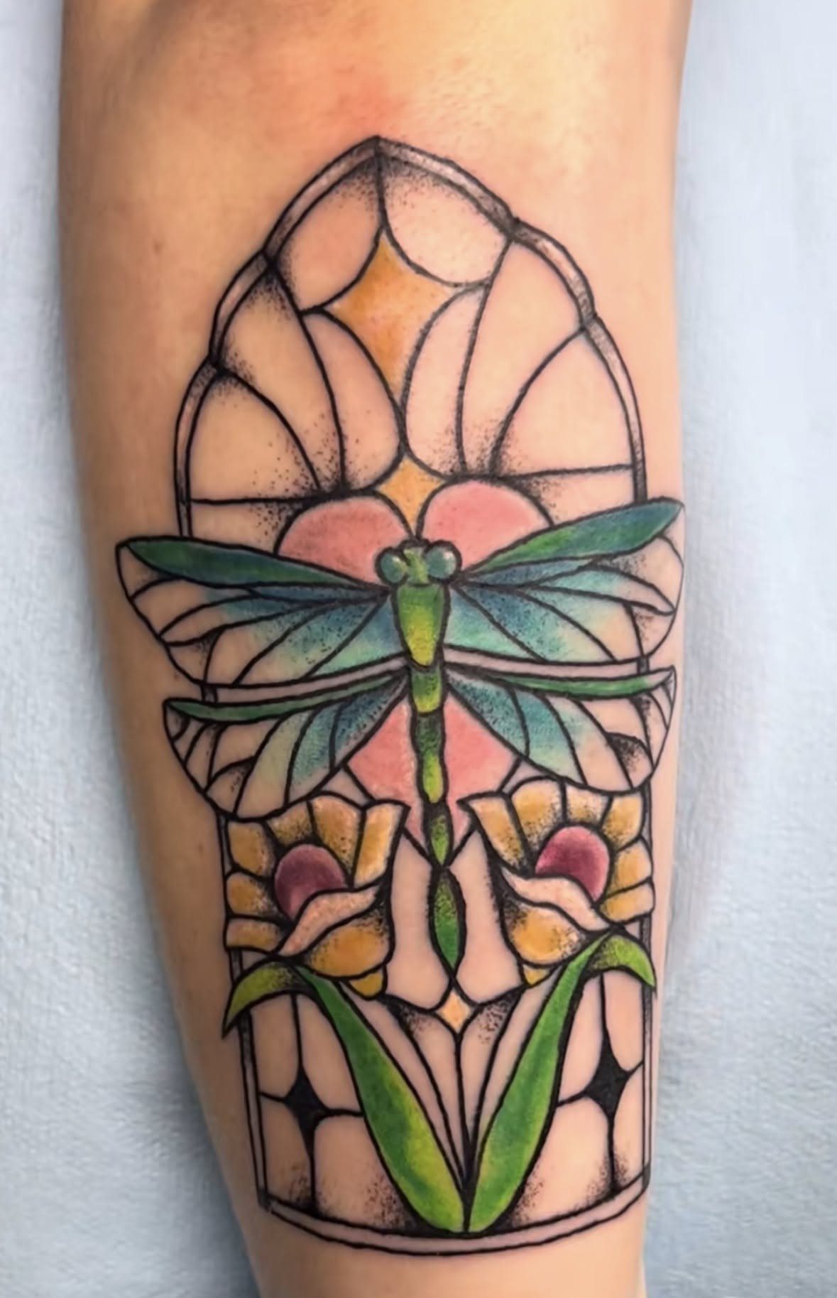 Dragonfly stained glass tattoo with colorful wings and flowers on a person's arm