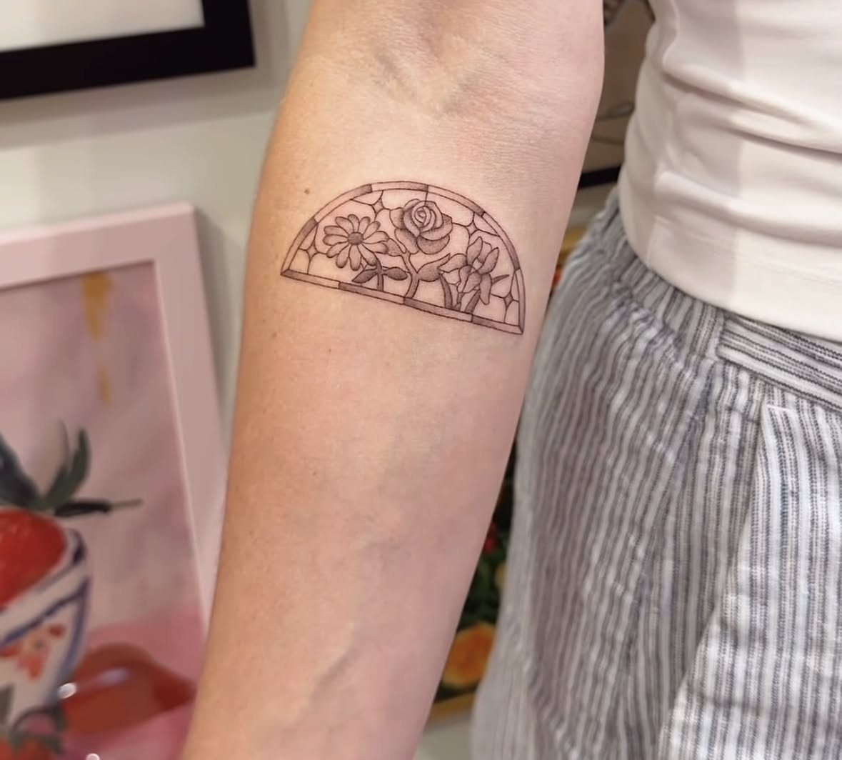 Stained glass window tattoo on a forearm featuring three stylized floral designs.