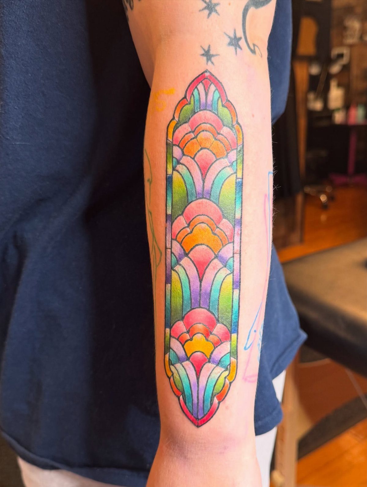 Colorful geometric stained glass tattoo with scalloped patterns on a person's forearm.