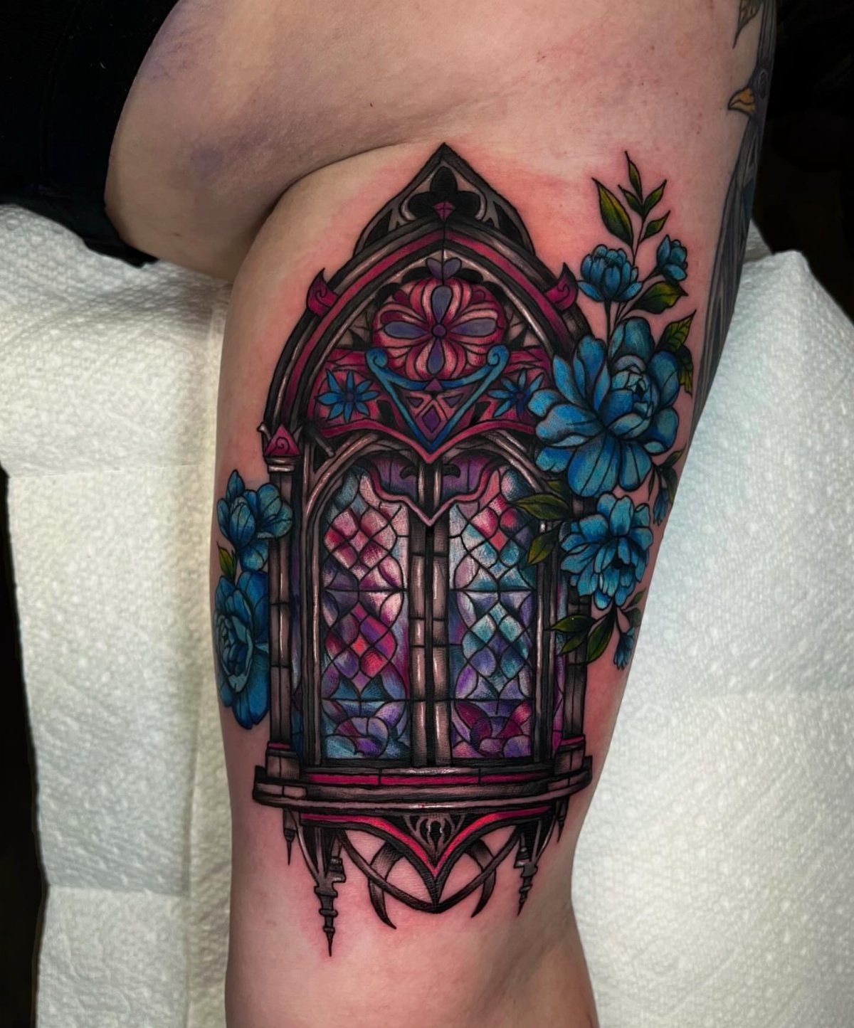 Gothic arch stained glass window tattoo with blue flowers on a leg
