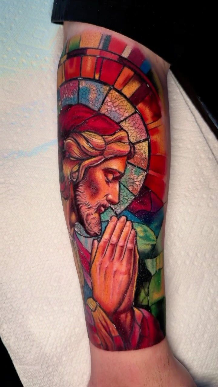 Jesus tattoo with praying hands in a colorful stained glass window style