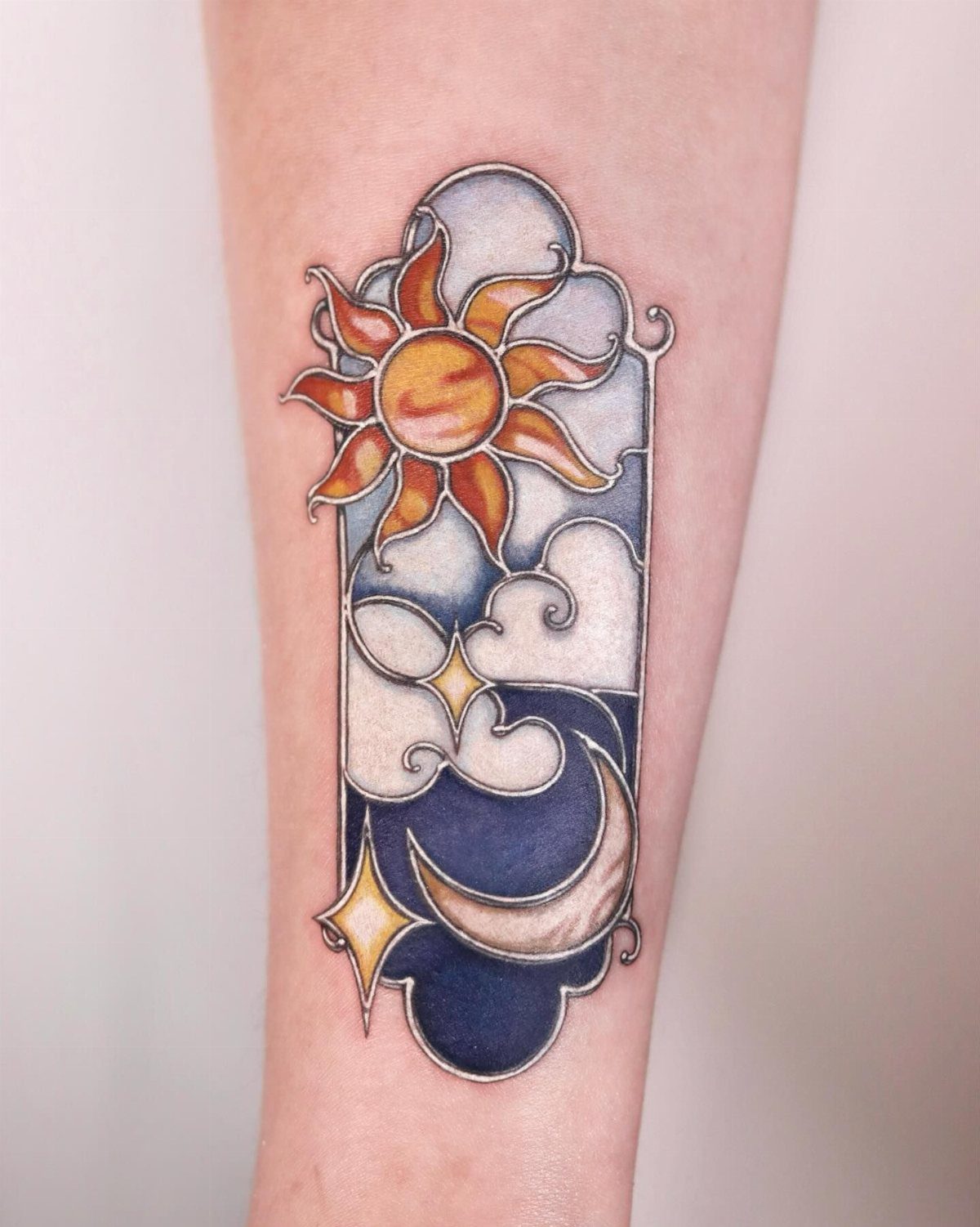 Stained glass tattoo of a sun and crescent moon on a person's arm
