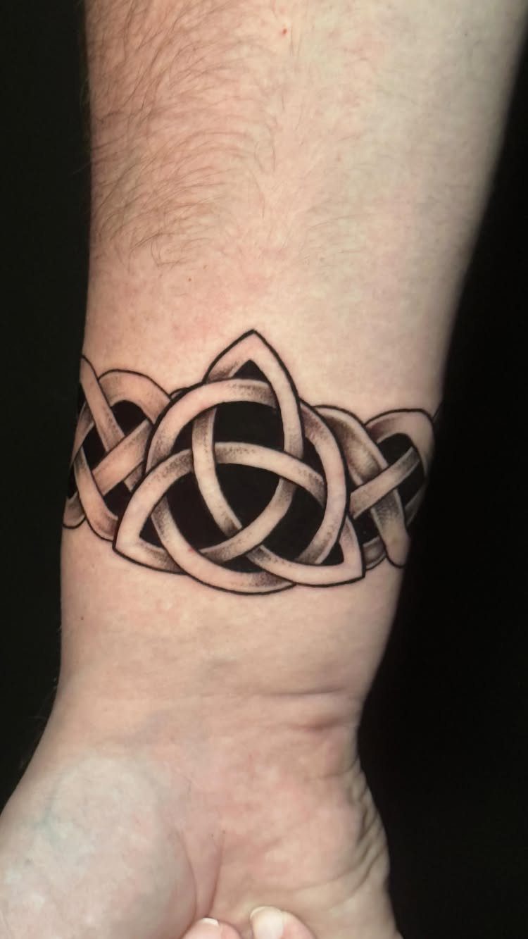 Celtic knot tattoo wrapped around a wrist in black and grey ink.