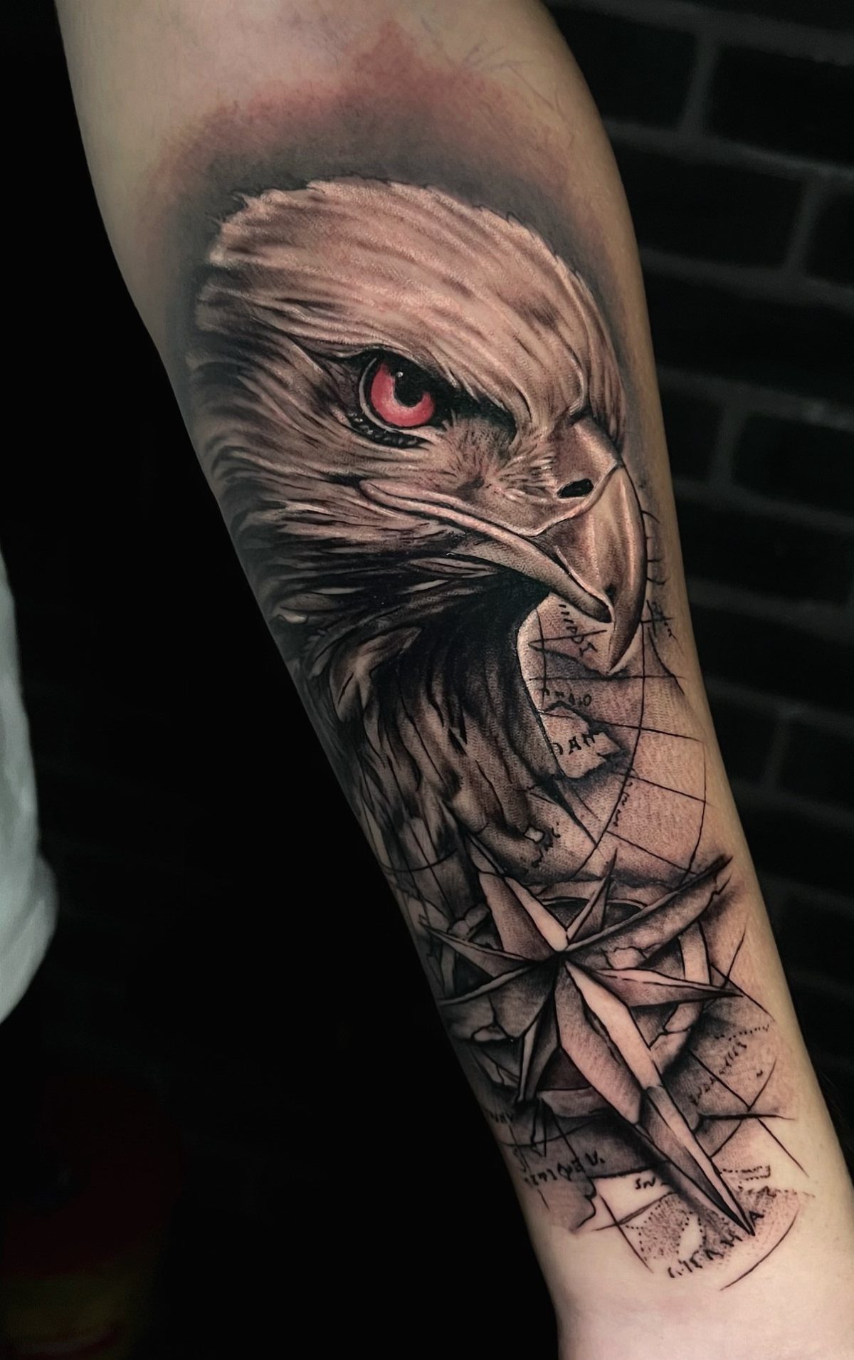 Bald eagle tattoo with red eye and compass rose on a forearm
