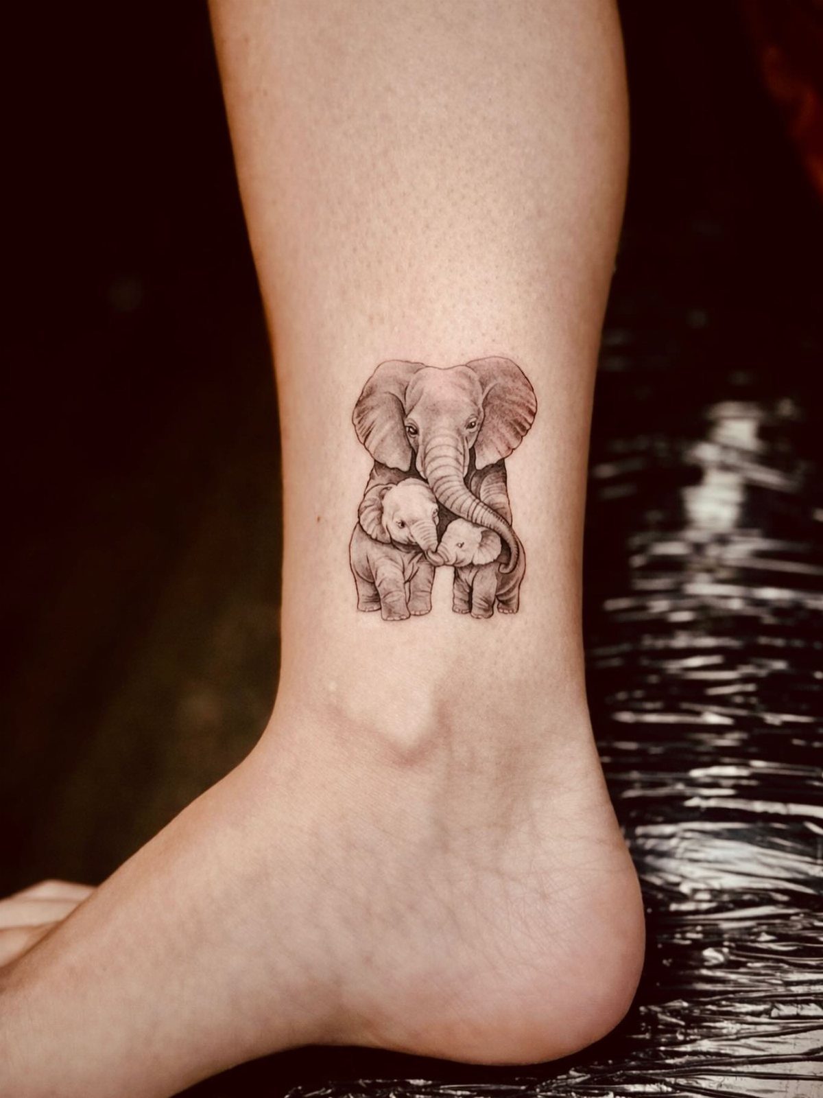 Elephant family tattoo on an ankle featuring an adult and two calves.