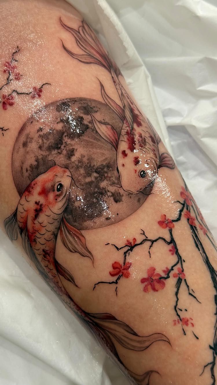 Two orange koi fish swimming around a moon with pink cherry blossoms tattoo.