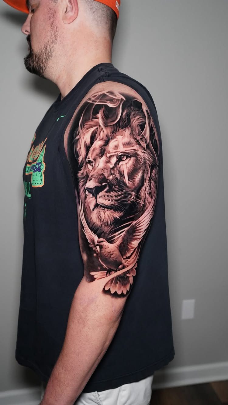 Lion and bird tattoo on a man's upper arm in realistic style.