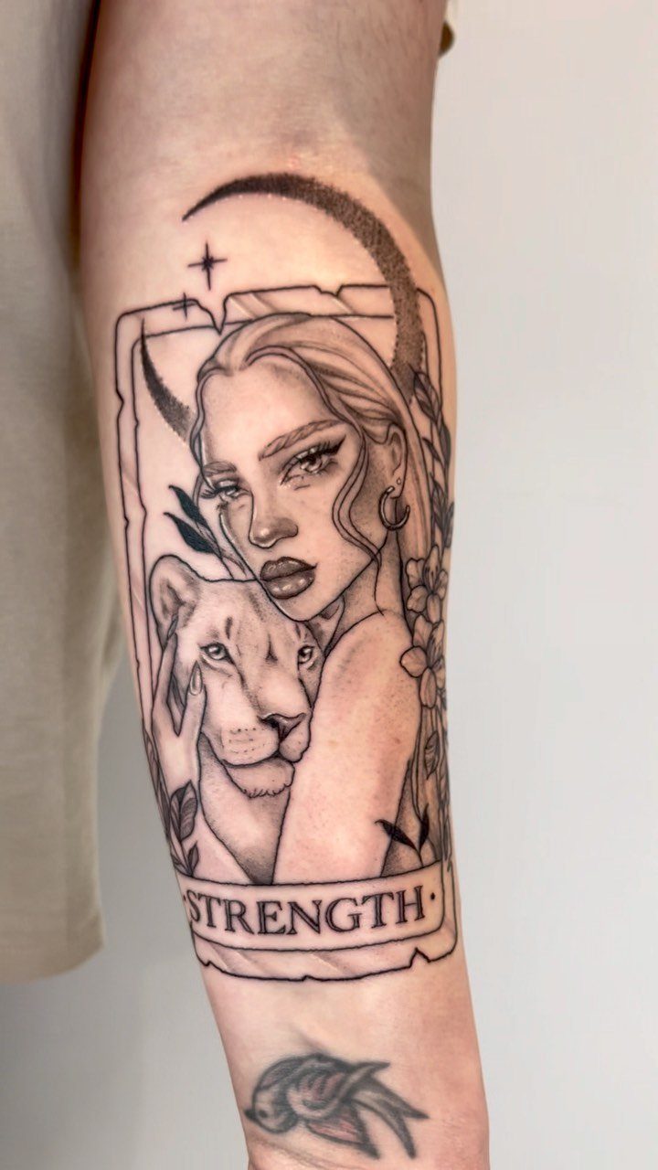Strength tarot card tattoo on a forearm featuring a woman and a lion