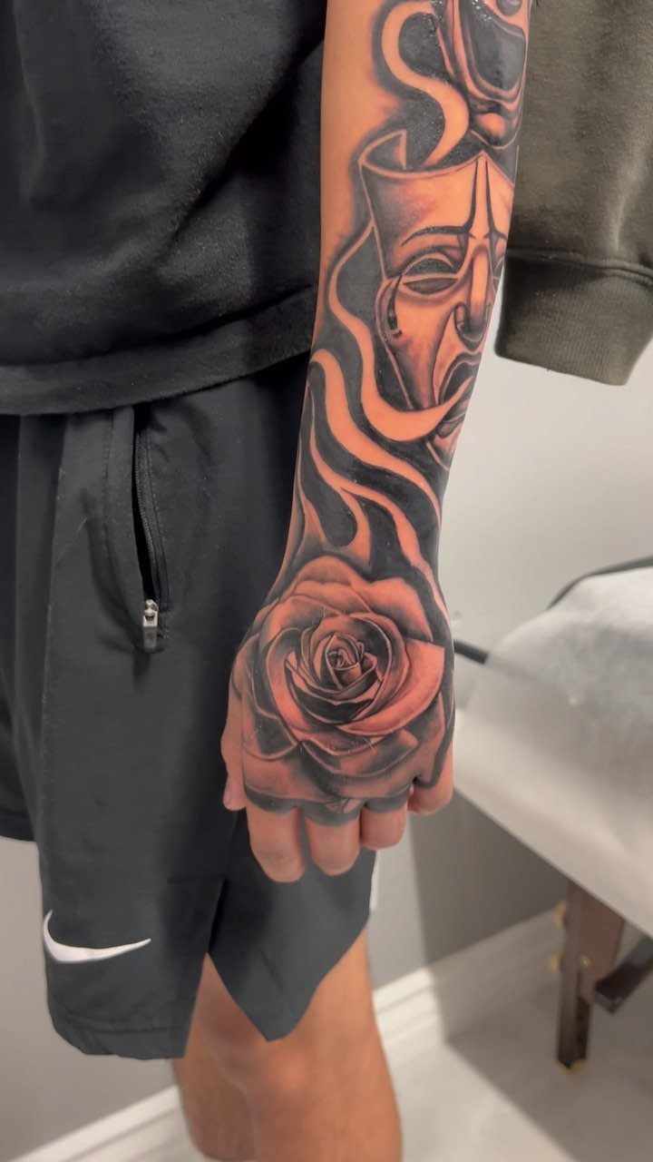 Black and gray tattoo of a rose on a person's hand and forearm.