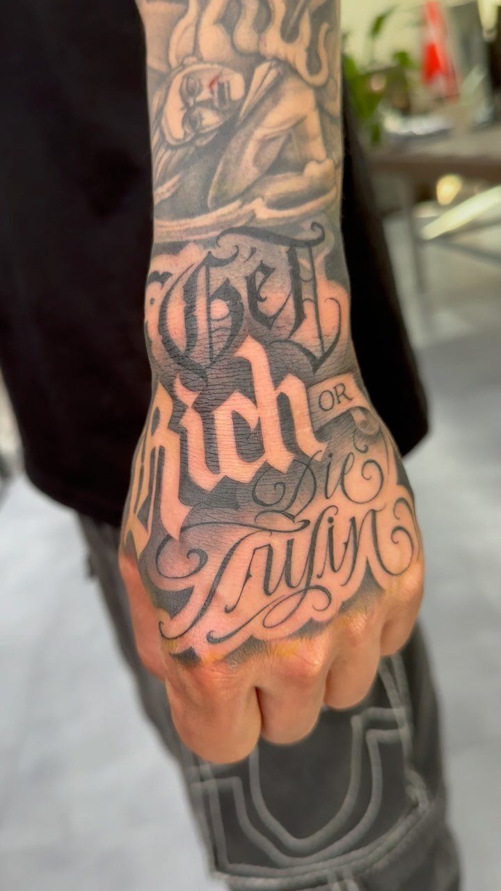 Hand and wrist with black and gray Chicano style script and portrait tattoos