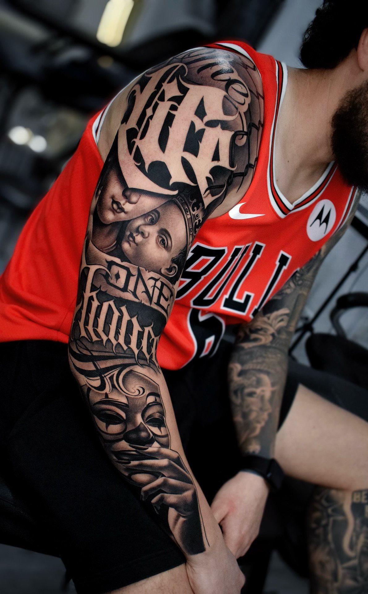 Detailed black-and-gray Chicano sleeve tattoo featuring portraits, script, and a payasa mask.