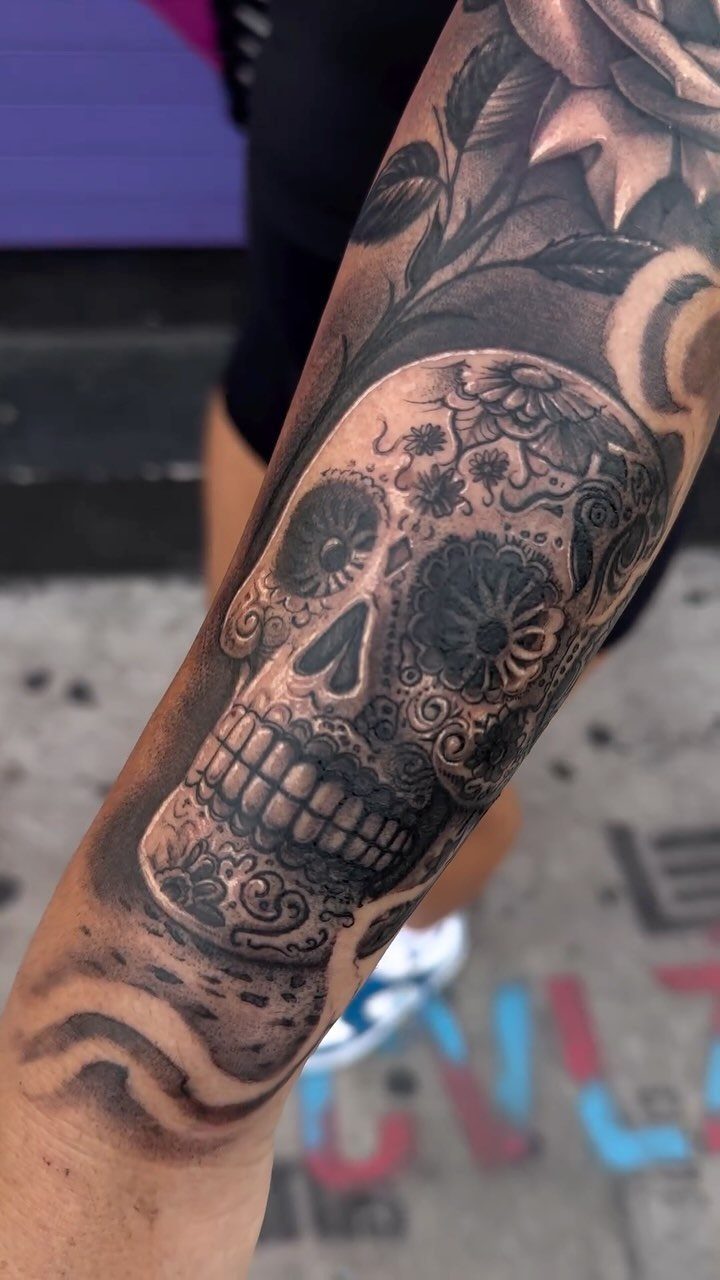 Day of the Dead sugar skull tattoo with roses on a person's arm