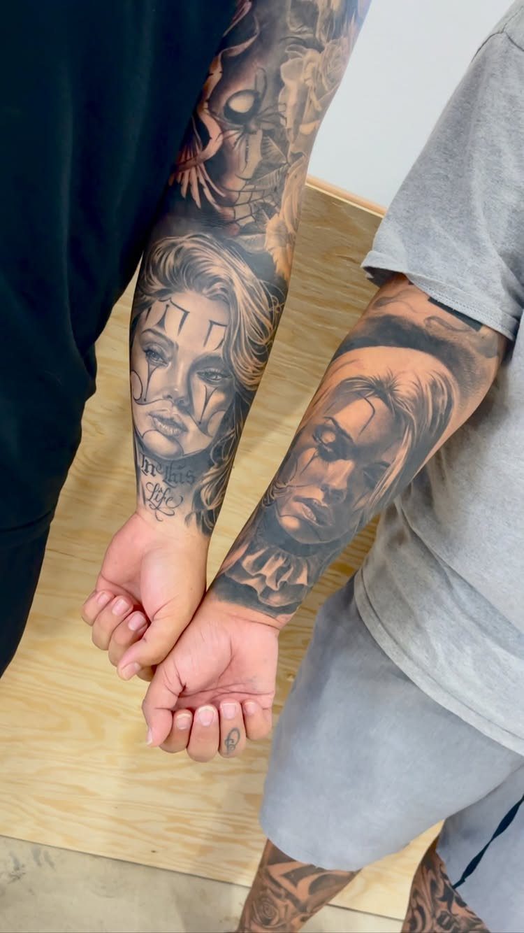 Two forearms featuring detailed black-and-gray Chicano tattoos of women with clown makeup.