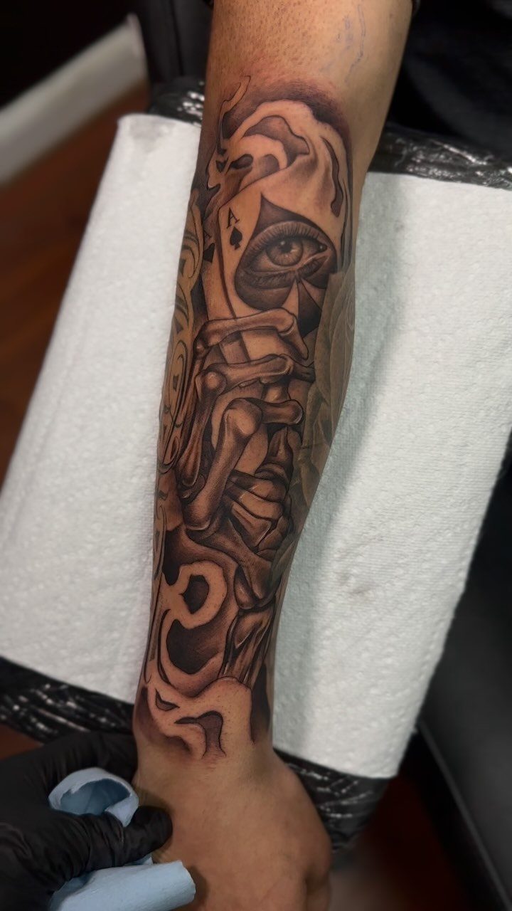 Half-sleeve black and gray tattoo on a forearm featuring an eye and skeletal hands.