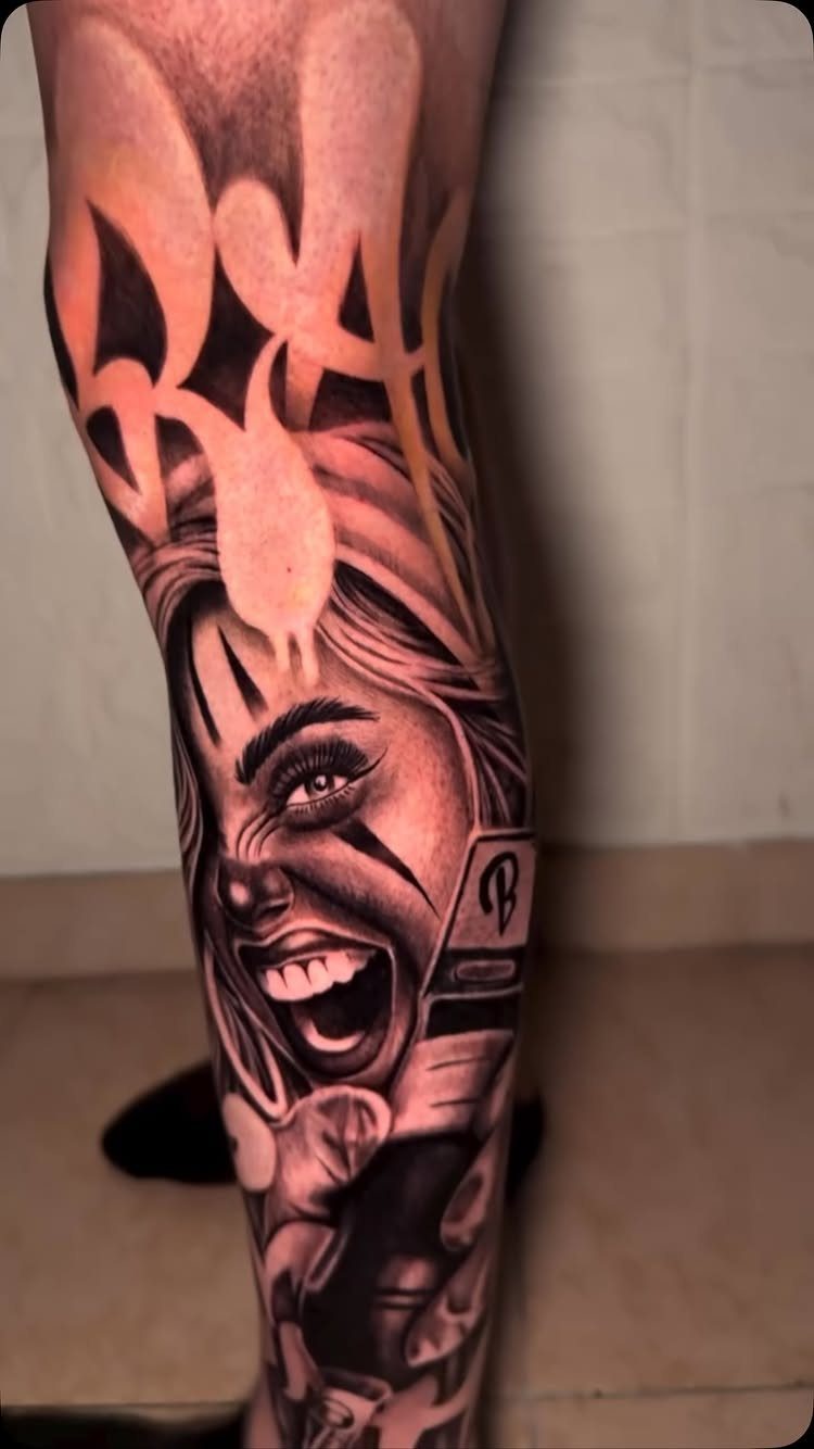 Leg tattoo of a laughing woman with clown makeup and stylized script lettering.