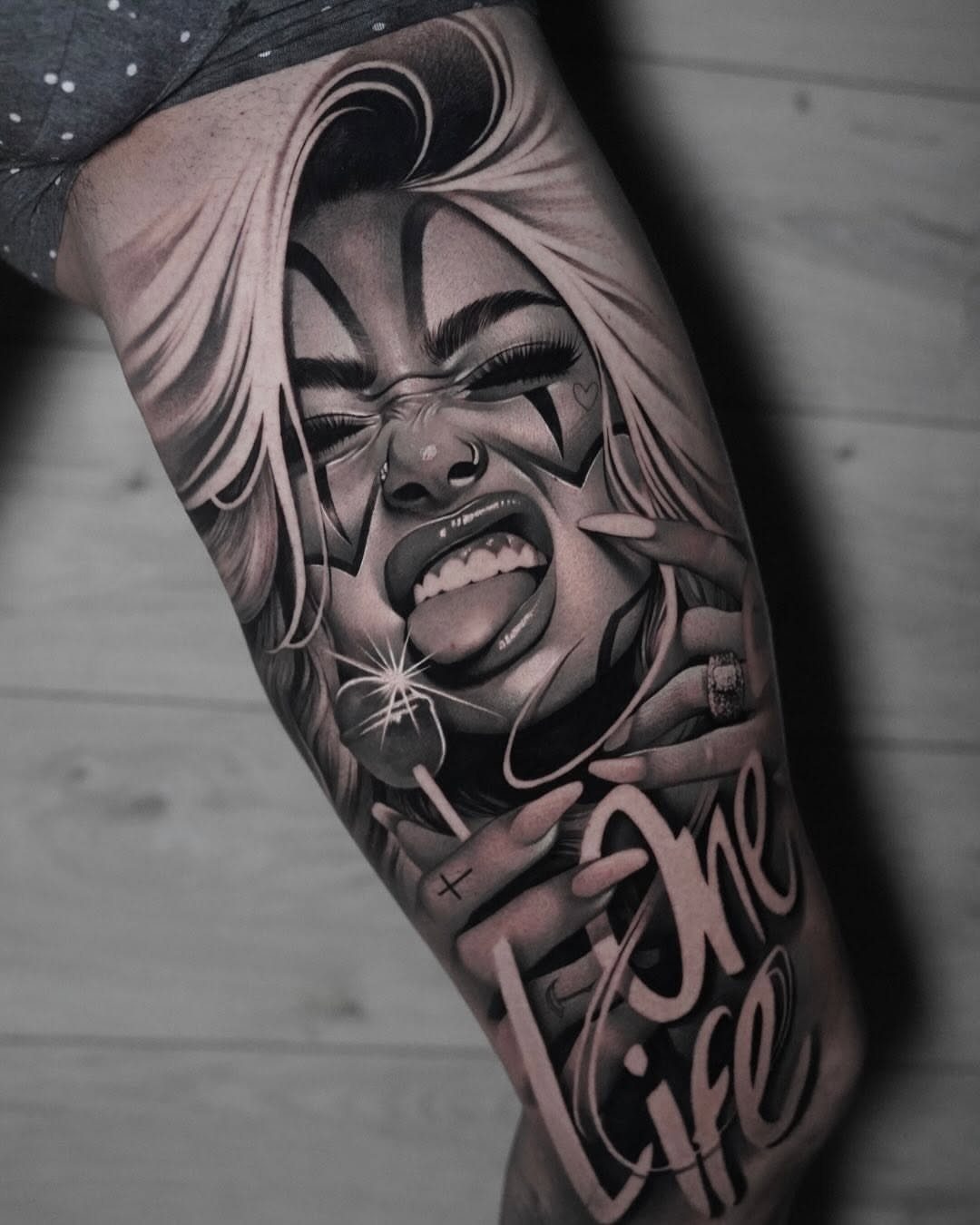 Black and gray tattoo of a woman with clown makeup and script lettering.
