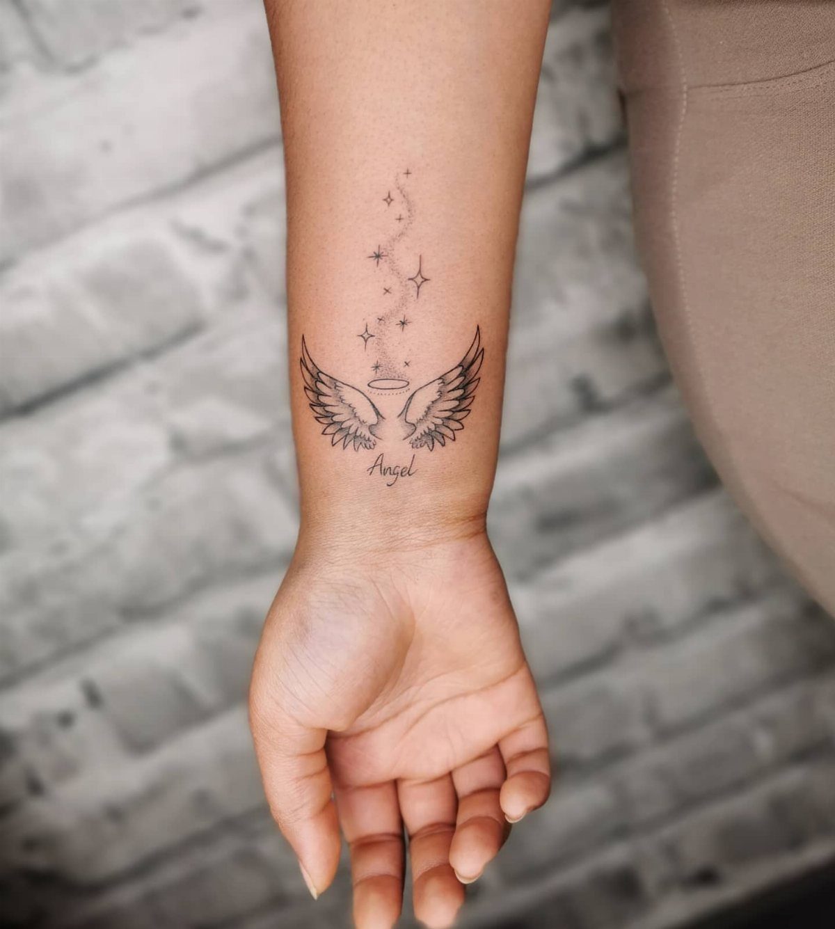 Angel wings tattoo with a halo and stars on a person's inner wrist.