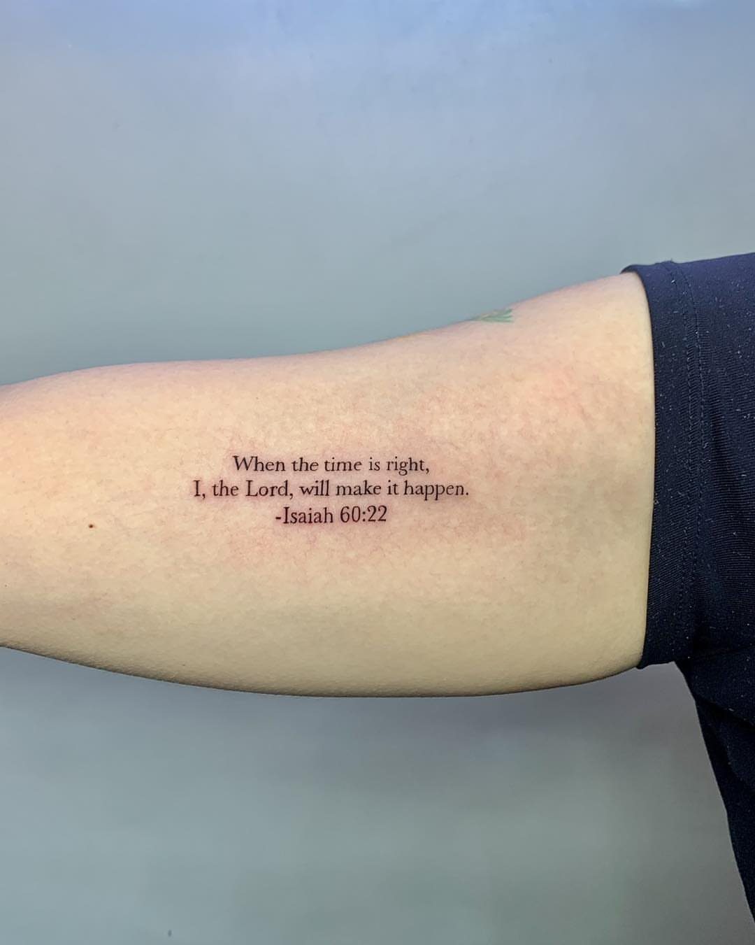 Forearm tattoo featuring a scripture verse from Isaiah 60:22 in black ink.