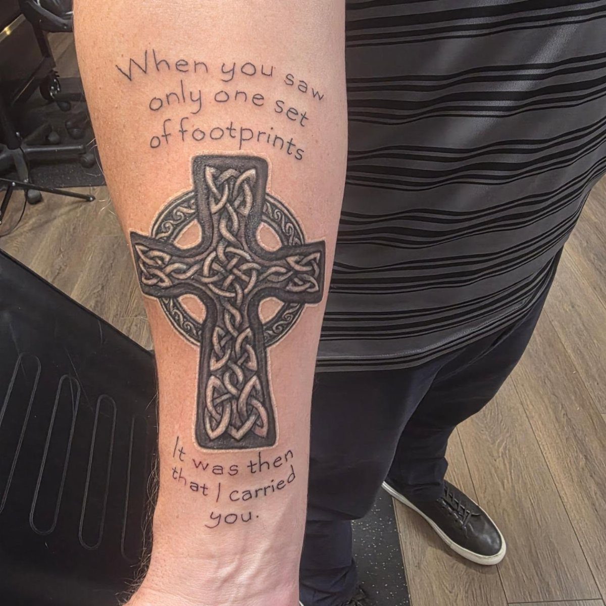 Celtic cross tattoo on a forearm with accompanying religious text about footprints.