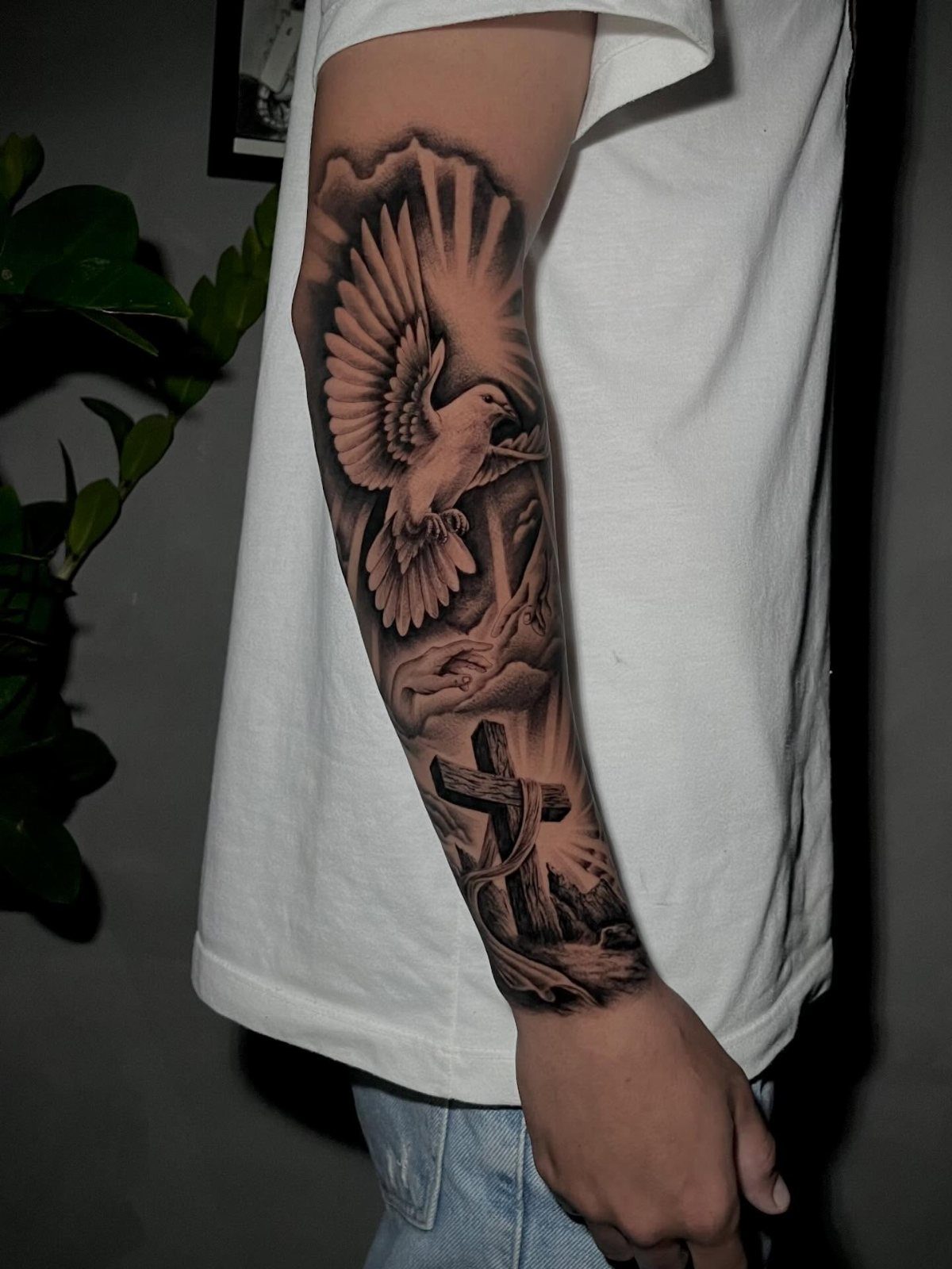 Forearm tattoo of a flying dove above a cross with radiating light beams.