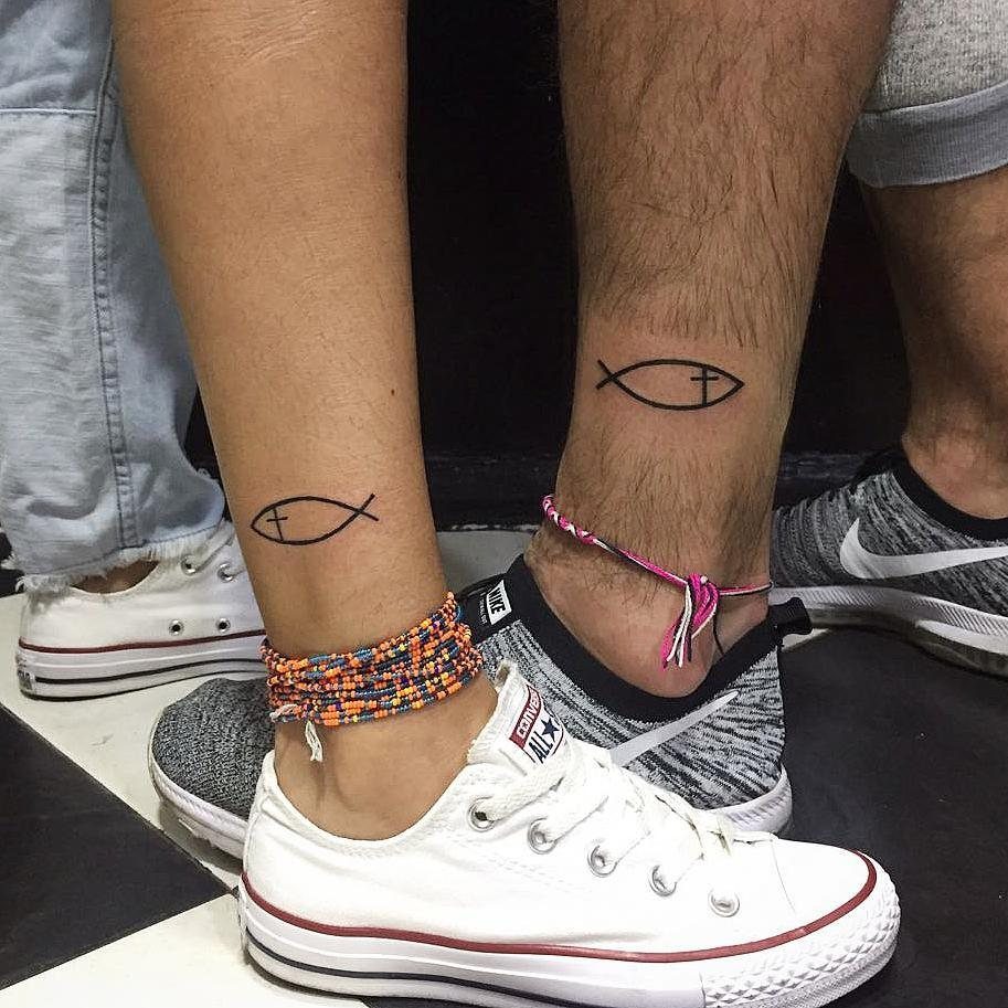 Two ankles with matching black Ichthys fish tattoos and casual sneakers.