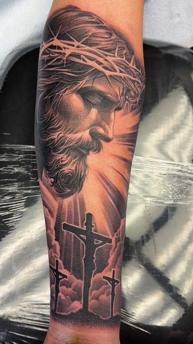 Jesus Christ tattoo with crown of thorns and three crosses on a forearm