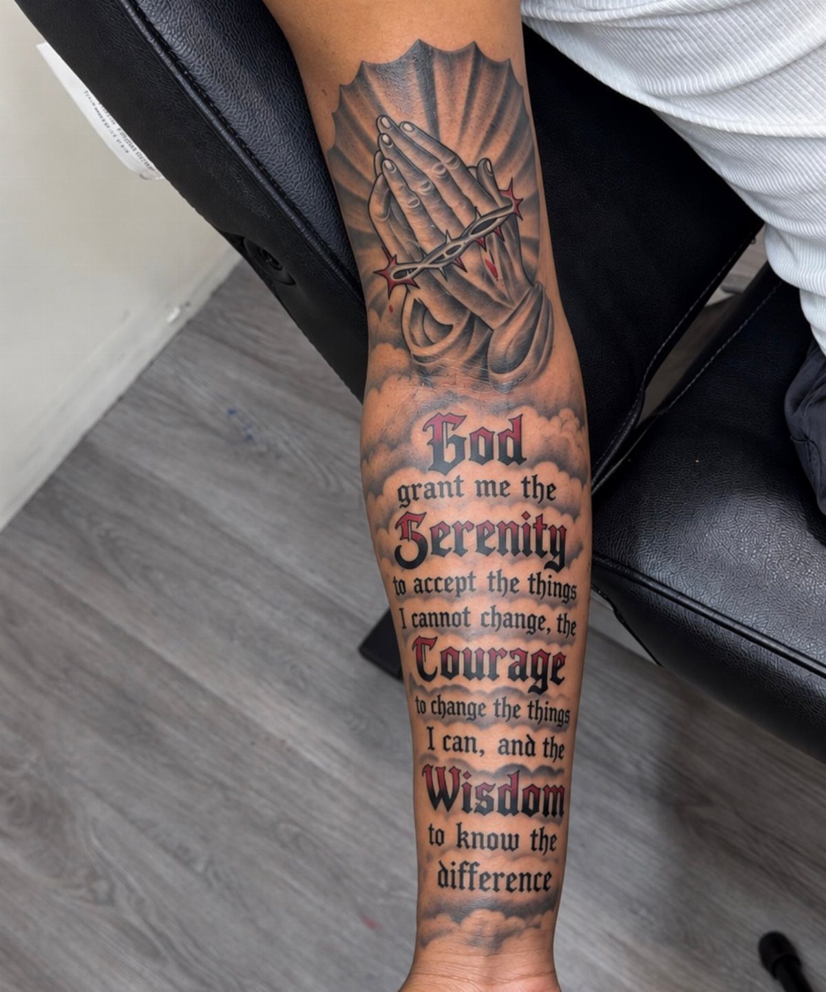 Praying hands tattoo with crown of thorns and the Serenity Prayer on forearm