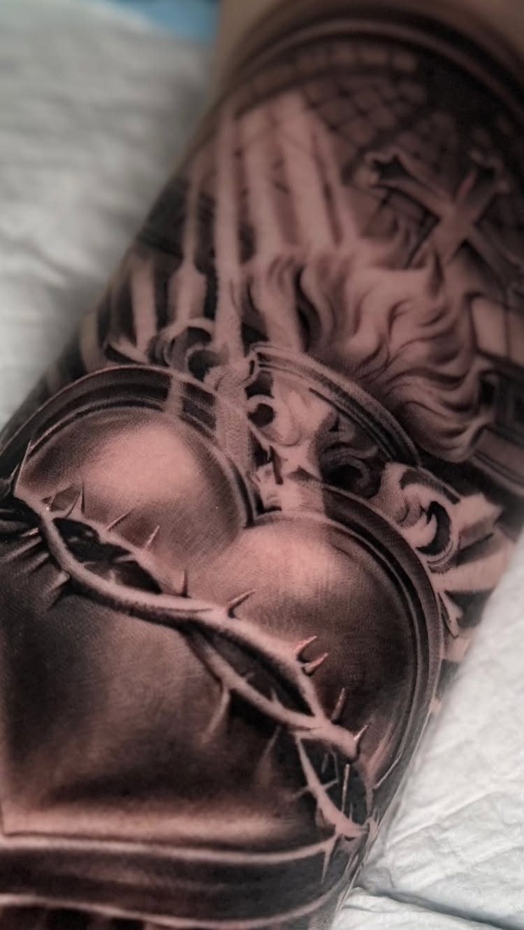Religious sleeve tattoo featuring a sacred heart with thorns and a cross.