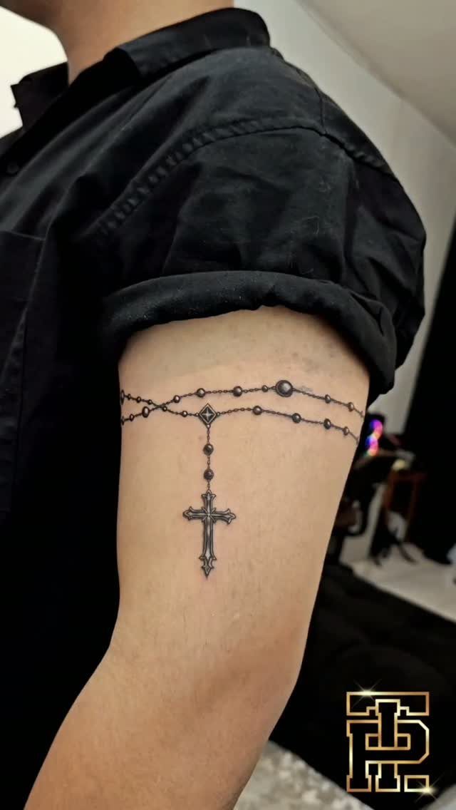 Rosary tattoo with beads and a cross wrapped around a man's upper arm.