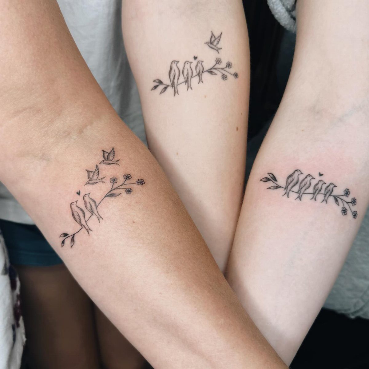 Matching bird tattoos on three forearms showing birds perched on a flowering branch