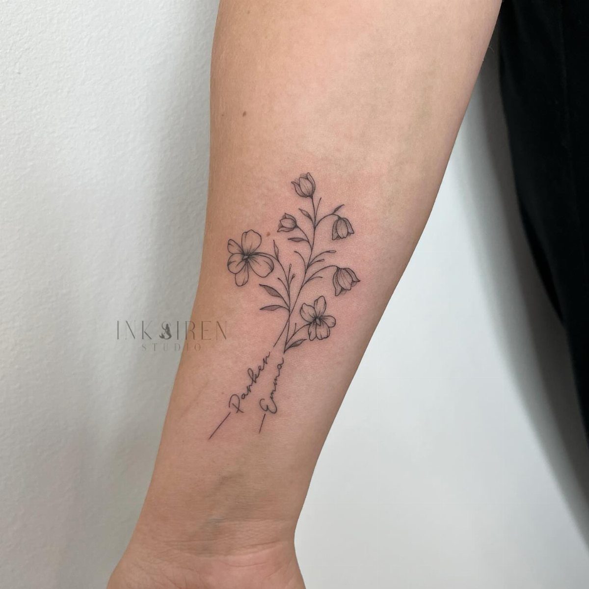 Floral tattoo on a forearm with delicate flowers and the names Parker and Emma.