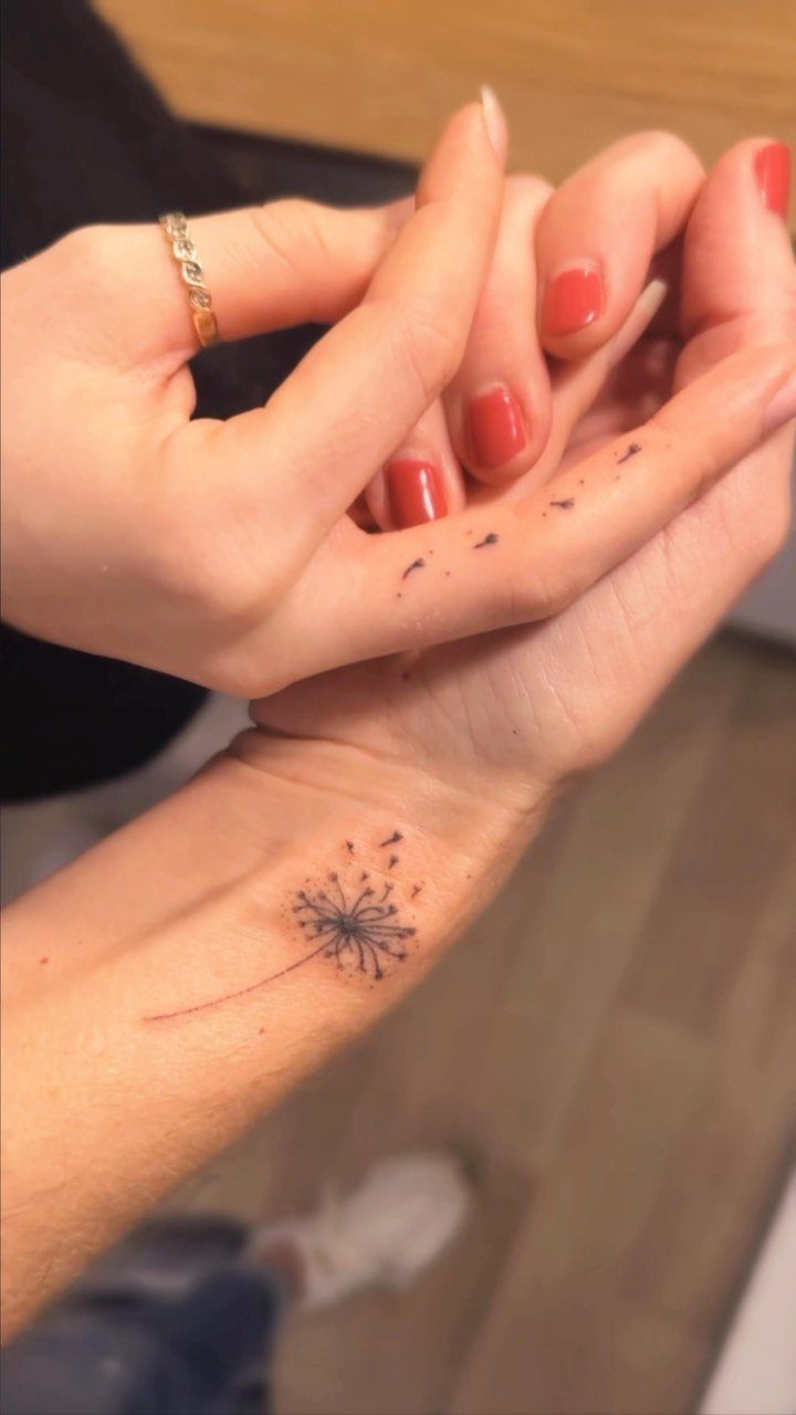 Dandelion tattoo on a wrist with matching floating seeds on another hand.
