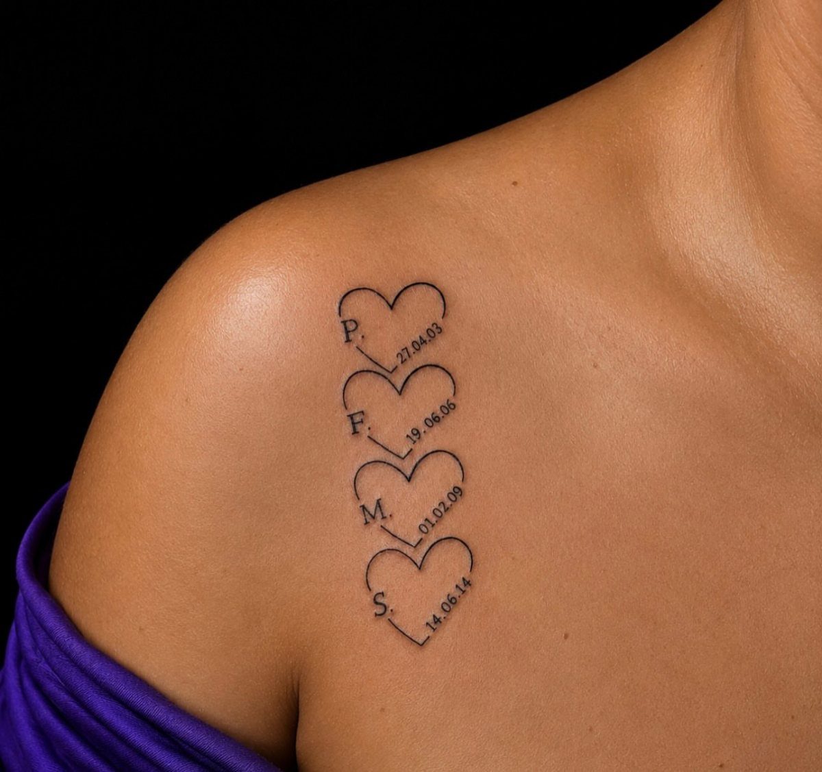 Four heart tattoos on a shoulder containing initials and dates in black ink.