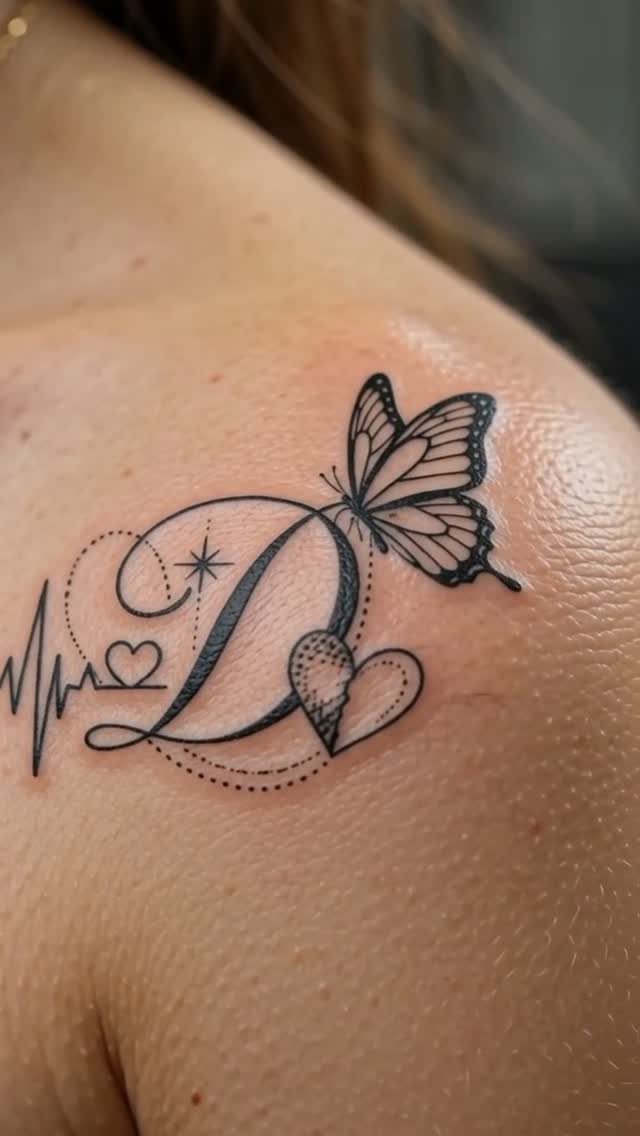 Tattoo on a shoulder featuring a cursive D, butterfly, and heartbeat line.